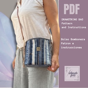 Könnte beinhalten: Eine Jeans-Kordelzugtasche mit einem braunen Lederriemen wird von einer Person gehalten. Die Tasche hat vertikale Streifen in verschiedenen Blautönen und weißer Spitze. Die Tasche hat ein kleines goldfarbenes rechteckiges Etikett. Der Text auf dem Bild lautet "PDF DRAWSTRING BAG Pattern and Instructions".