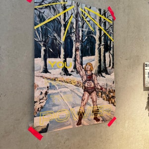 May include: An oil painting of a muscular figure holding a sword aloft in a snowy forest scene. The text "YOU HAVE THE POWER" is written in yellow. The artwork is affixed to a gray wall with red tape.