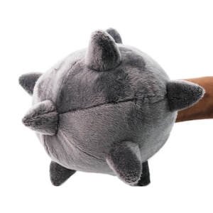 May include: A plush toy shaped like a spiked mace. The head of the mace is gray and fuzzy, with brown spikes. The handle is brown and fuzzy.