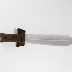Plush toy sword with a light gray blade and soft brown handle, shaped like a classic medieval weapon. Made from velvety fabric, it's perfect for imaginative play, costumes, or safe mock battles. Handcrafted by the GraTY Foundation – a Polish social enterprise supporting neurodivergent individuals and promoting inclusive employment through creative sewing workshops.