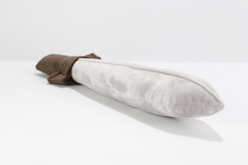 Close-up view of a soft plush toy sword lying on a white surface. The blade is made of light gray velvety fabric, and the hilt is crafted from a rich brown plush. The rounded tip and soft textures make it safe for children. Handmade by the GraTY Foundation—an inclusive social enterprise empowering neurodivergent creators through sewing and imaginative play.