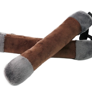 Puede incluir: Un par de juguetes de peluche para perros con forma de palo, de color marrón y gris. Los juguetes tienen una correa negra unida a un extremo.