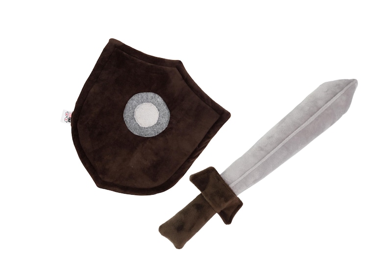 Plush sword and shield toy set on a white background. The sword features a soft gray blade with a brown handle and guard, while the shield is deep brown with a central gray circle and a visible fabric tag. Both items are handmade from soft, velvety materials, ideal for safe, imaginative play. This set is created by Fundacja GraTy, a social enterprise supporting neurodivergent makers and promoting inclusive, therapeutic play experiences.