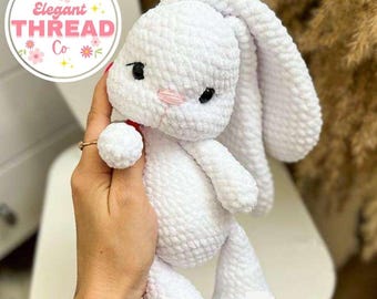 May include: White crocheted bunny rabbit amigurumi toy with long ears. The bunny has black eyes and a pink nose. The toy is being held by a hand.