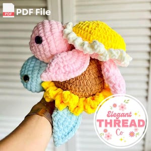 Op de afbeelding: Een gehaakt amigurumi-speelgoed in de vorm van een schildpad met een kleurenschema van roze, blauw, geel en bruin. De schildpad draagt een gele bloemenkroon. Het speelgoed wordt in de hand van een persoon gehouden. De afbeelding bevat de tekst "Elegant Thread Co."