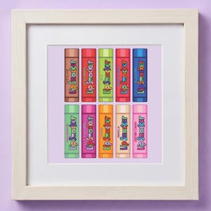 May include: A framed print showcasing a selection of Lip Smacker lip balm tubes. The tubes, each with a different flavour, are arranged in two rows. Flavours include Chocolate, Strawberry, Mint, and Blueberry, each with its own colour.