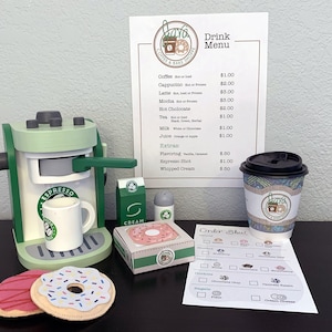 Puede incluir: Una máquina de espresso de juguete verde con una taza blanca, una caja de crema, una lata de crema batida y dos donuts. La máquina tiene un letrero que dice "Espresso". También hay un menú de papel con una lista de bebidas y precios. El menú dice "Drink Menu" y enumera artículos como "Coffee", "Cappuccino", "Latte", "Mocha", "Hot Chocolate", "Tea", "Milk", "Juice" y "Extras". El menú también enumera los precios de cada artículo. También hay una hoja de pedido de papel con una lista de donuts y coberturas.