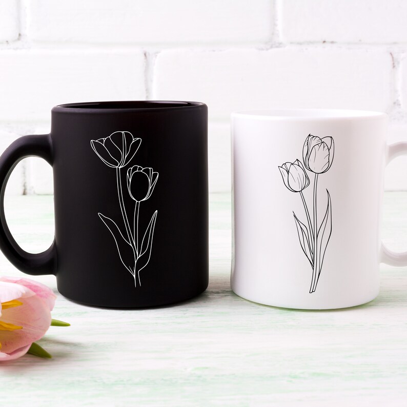 May include: Two ceramic mugs with a simple line drawing of tulips. One mug is black with white tulips, the other is white with black tulips.