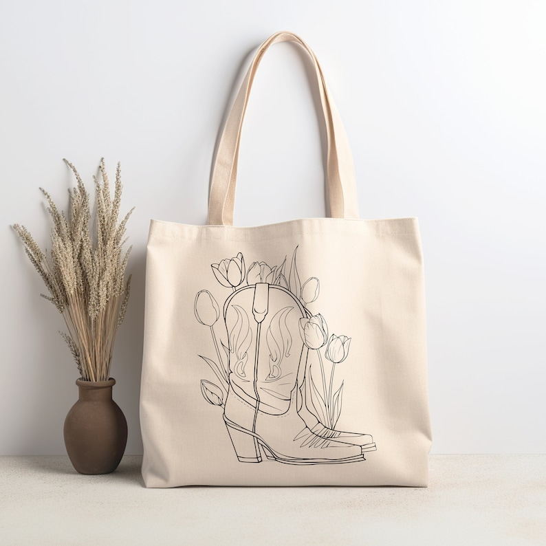 May include: A white canvas tote bag with a black line drawing of cowboy boots and tulips. The boots are in the center of the bag and the tulips are on either side of the boots.