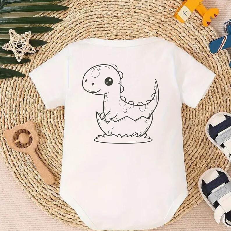 May include: White baby onesie with a black and white illustration of a dinosaur hatching from an egg.