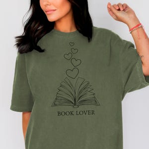 May include: A green t-shirt with a black graphic of an open book with hearts floating above it. The text "BOOK LOVER" is printed below the book.