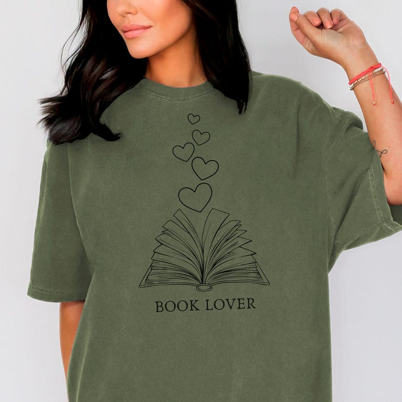 May include: A green t-shirt with a black graphic of an open book with hearts floating above it. The text "BOOK LOVER" is printed below the book.