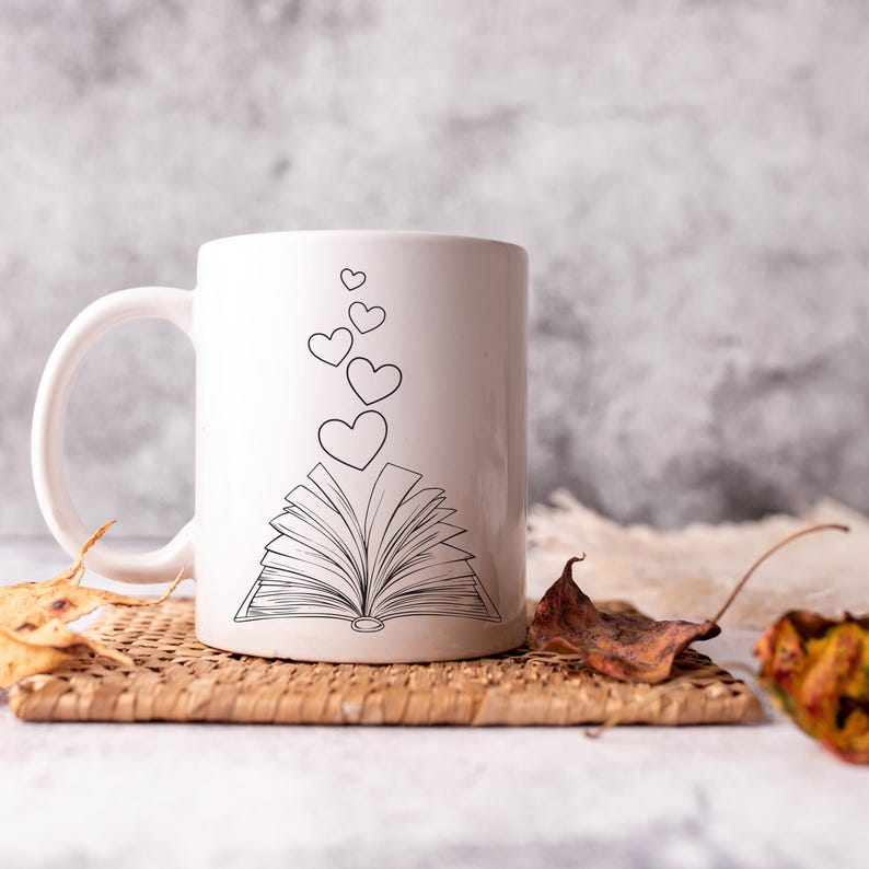 May include: White ceramic mug with a black outline of an open book with hearts floating above it.