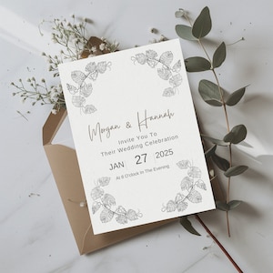 K&ouml;nnte beinhalten: Eine wei&szlig;e Hochzeitseinladung mit floralem Rand. Die Einladung lautet "Morgan & Hannah Invite You To Their Wedding Celebration JAN 27 2025 At 8 O'clock In The Evening".
