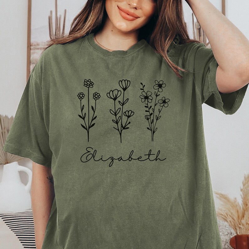 May include: A green t-shirt with a floral design and the name "Elizabeth" printed on the front.