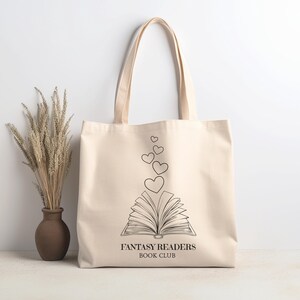 May include: A beige canvas tote bag with black text that reads "Fantasy Readers Book Club". The bag features a black line drawing of an open book with hearts floating above it.