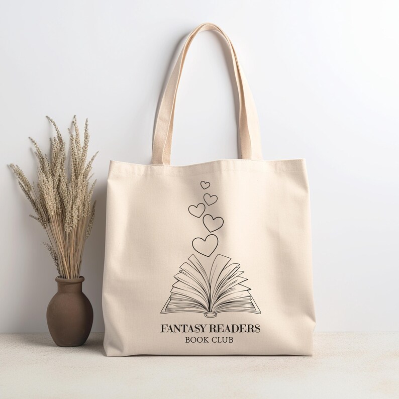 May include: A beige canvas tote bag with black text that reads "Fantasy Readers Book Club". The bag features a black line drawing of an open book with hearts floating above it.