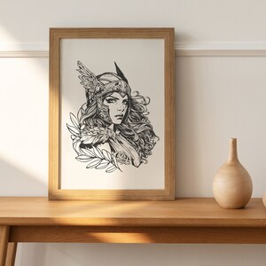 May include: A black and white line art print of a woman wearing a helmet with wings and a flowing cape. The print is framed in a light brown wood frame.