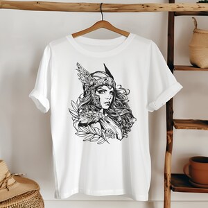 May include: White t-shirt with a black and white illustration of a woman wearing a helmet with wings and a flowing cape.