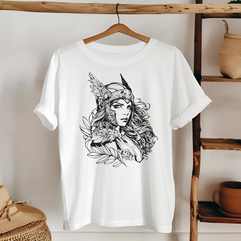 May include: White t-shirt with a black and white illustration of a woman wearing a helmet with wings and a flowing cape.