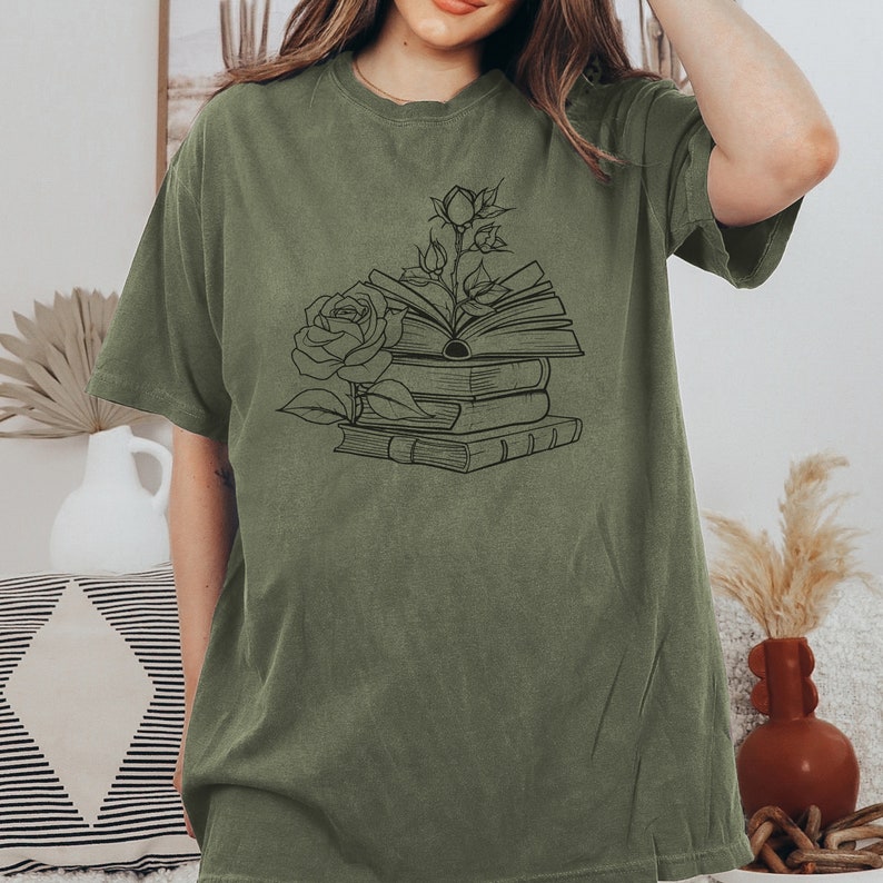 May include: A green t-shirt with a black line drawing of a stack of books with a rose growing out of the top book.