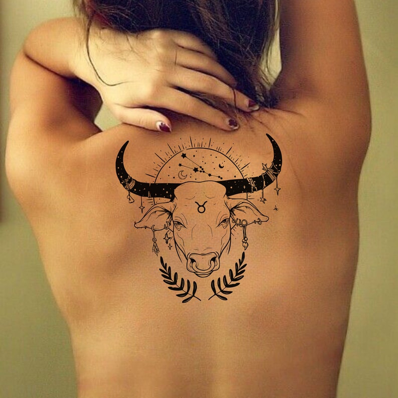 May include: A black and white line art tattoo design of a bull's head with a constellation and a crescent moon above it. The bull's head is surrounded by a circle with stars and a Taurus symbol.