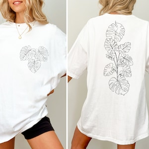 K&ouml;nnte beinhalten: Wei&szlig;es Oversize-T-Shirt mit einer schwarzen Linienzeichnung von tropischen Bl&auml;ttern auf Vorder- und R&uuml;ckseite.
