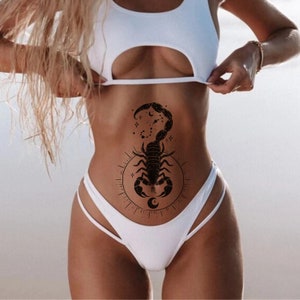 May include: A black scorpion tattoo with a crescent moon and stars on a person's stomach.