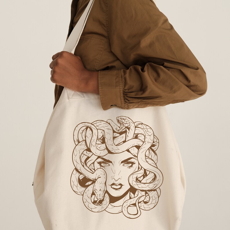 May include: A white canvas tote bag with a brown line drawing of Medusa, a woman with snakes for hair, on the front.