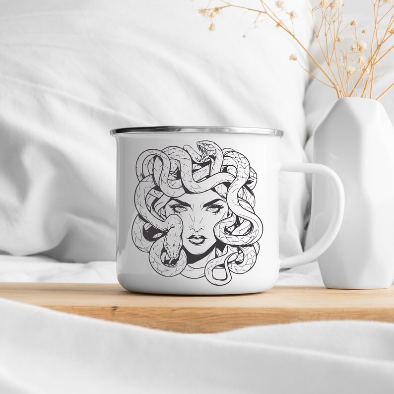 May include: White enamel mug with a black and white illustration of Medusa, a woman with snakes for hair.