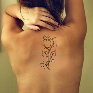 May include: A line drawing of a rose tattoo on a person's back.