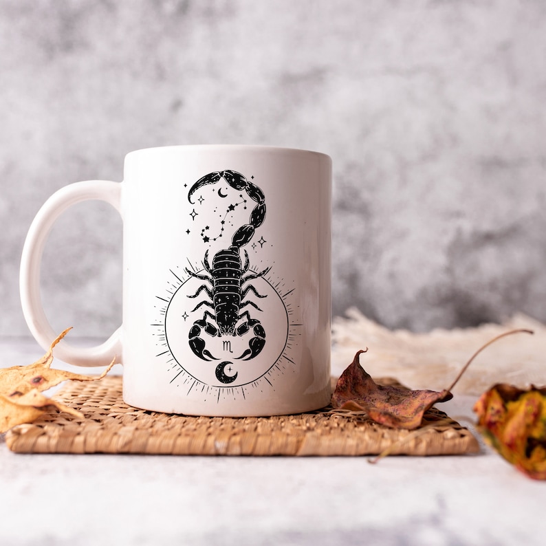 May include: White ceramic mug with a black scorpion design. The scorpion is surrounded by stars and a crescent moon. The mug has the astrological symbol for Scorpio, "m", and a crescent moon.