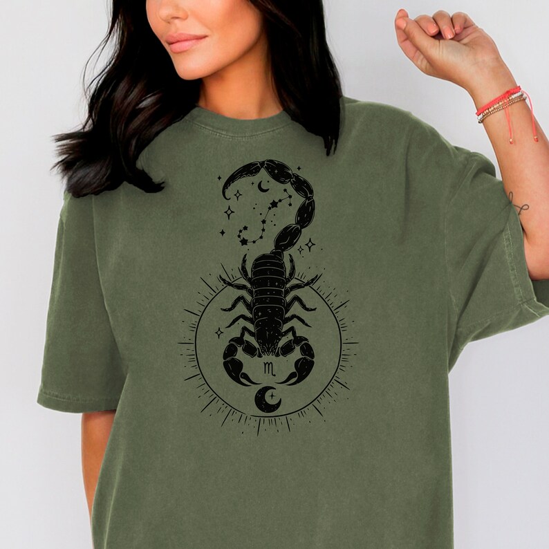 May include: A green t-shirt with a black scorpion design. The scorpion is surrounded by stars and a crescent moon. The letter "m" is in the center of the design.
