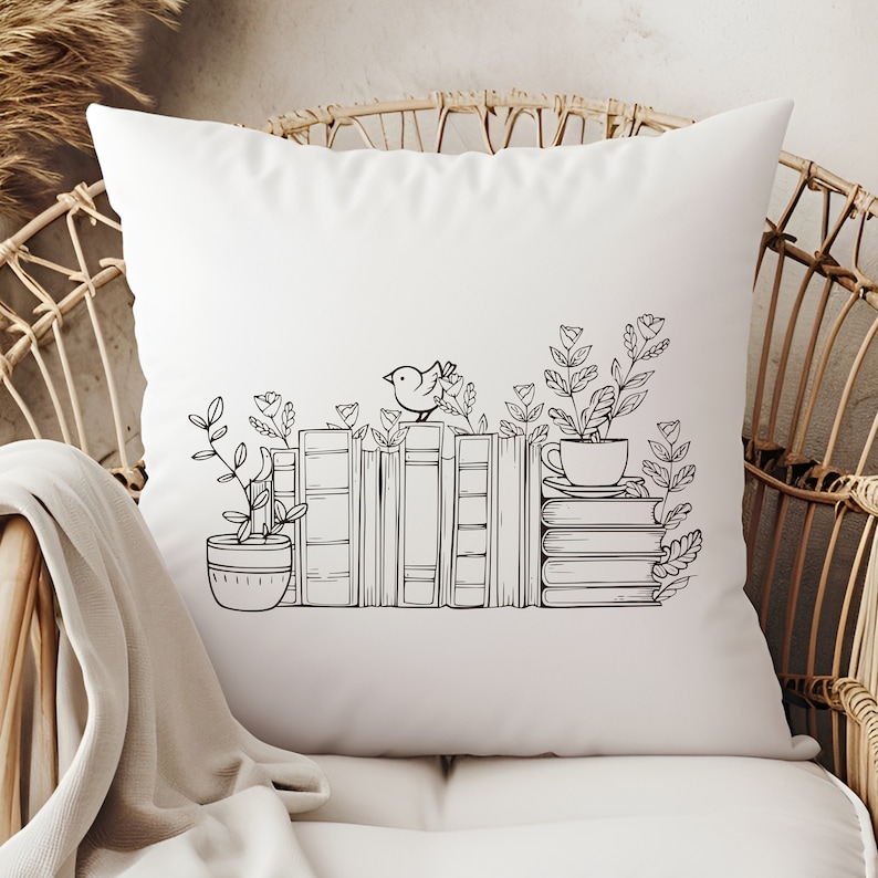May include: A white throw pillow with a black and white illustration of a stack of books, a bird, a cup, and plants. The illustration is centered on the pillow.