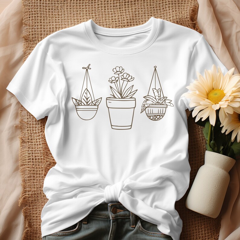 May include: White t-shirt with a graphic of three potted plants. The plants are drawn in a simple line style and are hanging from the ceiling.