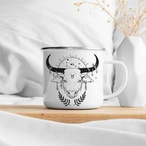 May include: White enamel mug with a black and white illustration of a bull's head with a Taurus zodiac symbol and celestial details. The mug has a silver rim and handle.