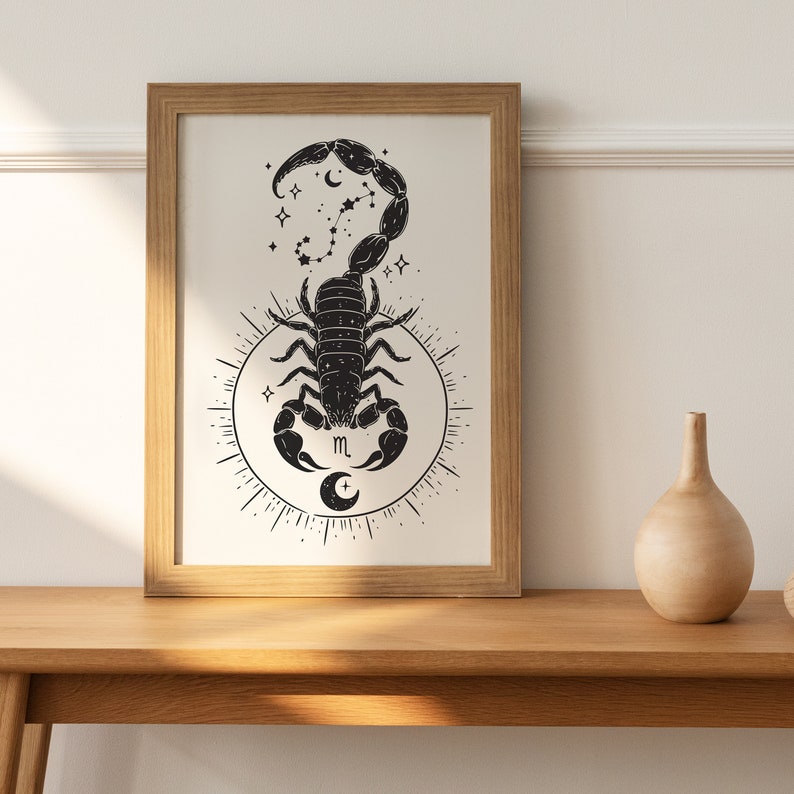 May include: A black and white illustration of a scorpion with a crescent moon and stars. The scorpion is surrounded by a circle with a crescent moon and the letter "m" in the center. The illustration is framed in a light brown wood frame.