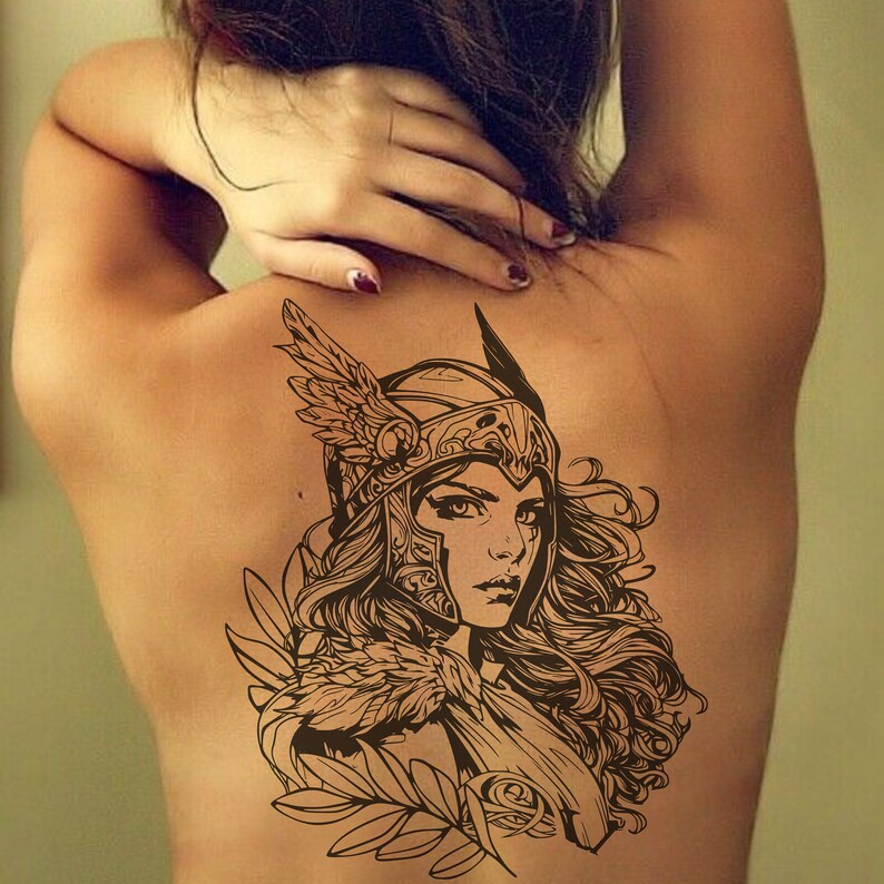 May include: A black and white line art tattoo design of a woman wearing a winged helmet and armor. The design features intricate details and a flowing hairstyle.