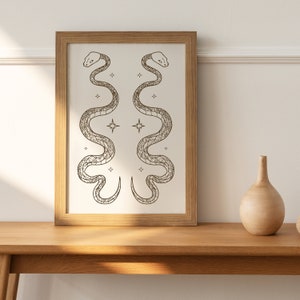 May include: A framed print of two stylised snakes with intricate patterns, facing each other, with a background of small stars.