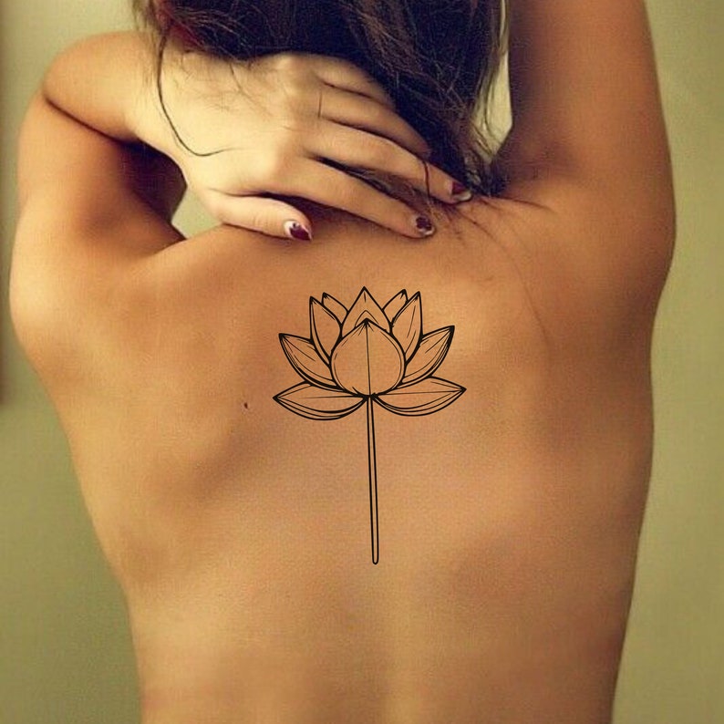 May include: A simple line drawing of a lotus flower tattoo on a person's back.