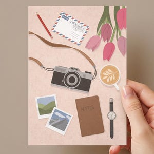 Könnte beinhalten: Eine flache Illustration auf hellrosa Hintergrund mit einer schwarzen Kamera mit braunem Riemen, einem roten Stift, einem Umschlag mit blau-rotem Rand, rosa Tulpen, einer Tasse Latte, zwei quadratischen Landschaftsfotos, einem braunen Notizbuch und einer Armbanduhr.