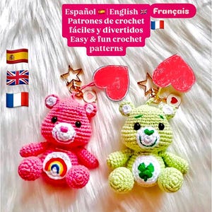 Può includere: Due portachiavi a forma di orsetto all'uncinetto. Uno è rosa con la pancia arcobaleno, l'altro è verde con un quadrifoglio. Entrambi hanno ciondoli a forma di stella e cuore dorati. L'immagine include il testo in spagnolo, inglese e francese: "Easy & fun crochet patterns."