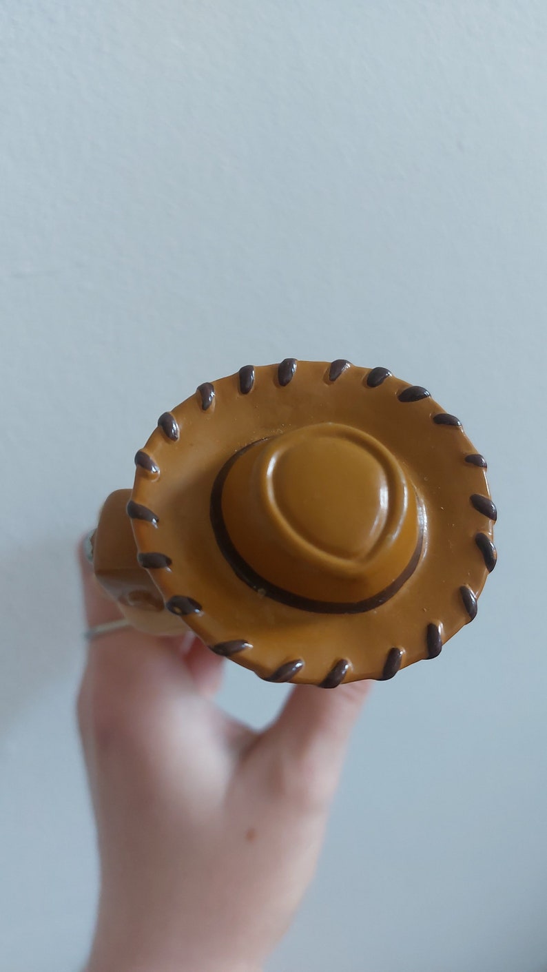 May include: A close-up of a tan cowboy hat with a brown brim and stitching detail. The hat has a rounded crown and a wide brim, with a dark brown stitched border. The hat is a toy or collectible item.