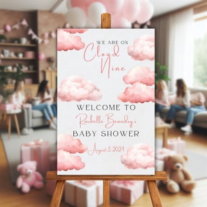May include: A pink and white baby shower welcome sign with watercolor clouds and the text "We are on Cloud Nine. Welcome to Rachelle Beaudry's Baby Shower. August 3, 2024."