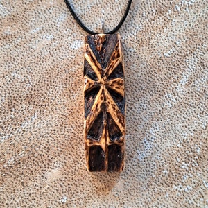 May include: A wooden pendant necklace with a black cord. The pendant is carved with a geometric design and has a dark brown finish.