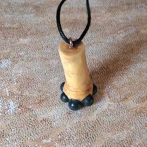 May include: A pendant necklace with a light-coloured, cylindrical charm and a cluster of dark blue-black beads at the base. The charm hangs from a black cord necklace.