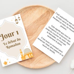 以下が含まれることがあります： フランス語のテキストが書かれた2枚のカード。1枚は「Jour 1 Le d&eacute;but du Ramadan」と三日月と星のデザイン。もう1枚はラマダンについてのテキストです。カードは木製のプレートの上にあります。