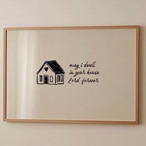 Può includere: Stampa incorniciata con un'illustrazione di una casa disegnata a mano e la scritta «may i dwell in your house Lord. forever». La casa è in bianco e nero. La cornice è marrone chiaro.