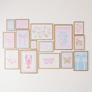 Pode incluir: Uma coleção de impressões de arte emolduradas em vários tamanhos, com designs em rosa pastel e azul. As impressões incluem borboletas, uma lagosta, um laço e textos que dizem "You're Cute" e "Today is going to be a good day!"