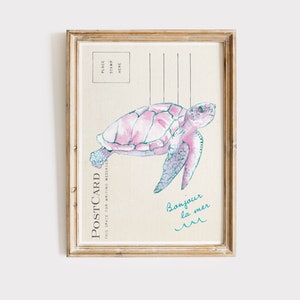 May include: A framed postcard print featuring a watercolor illustration of a pink sea turtle. The postcard has a vintage aesthetic with the word "POSTCARD" printed on the left side and the phrase "Bonjour la mer" in teal.